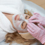 Facial peeling mask, beauty spa, skin care. Woman getting facial treatment by beautician at SPA salon, closeup